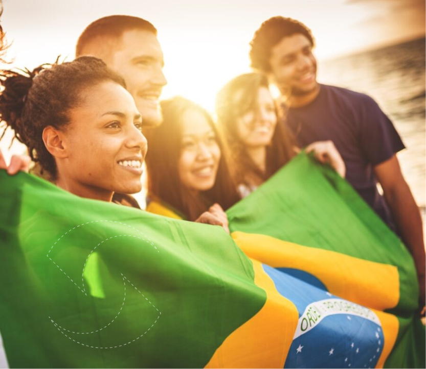 Jovens sorridentes segurando a bandeira do brasil com o brilho do sol por trás