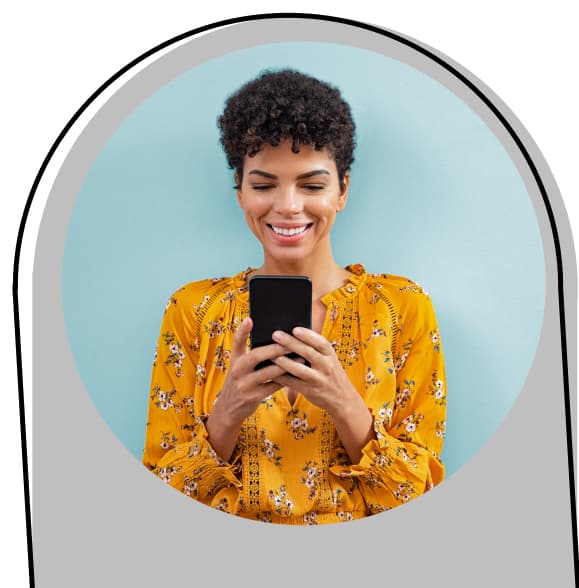 Mulher negra de cabelo curto sorri ao olhar para a tela do celular em suas mãos