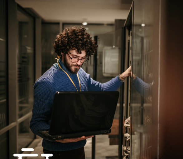 Homem segurando um laptop na mão trabalha em um dos servidores do data center